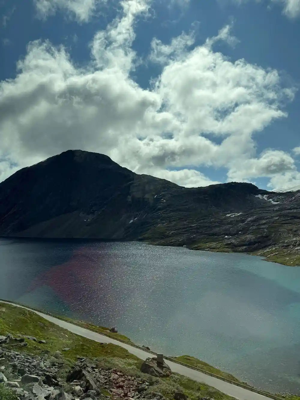 Alpine lake with dark water beneath mountain under sky
