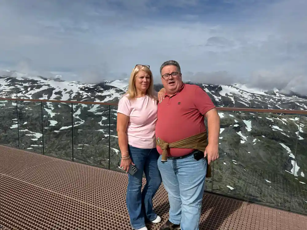 Couple on viewing platform overlooking green valley fjord