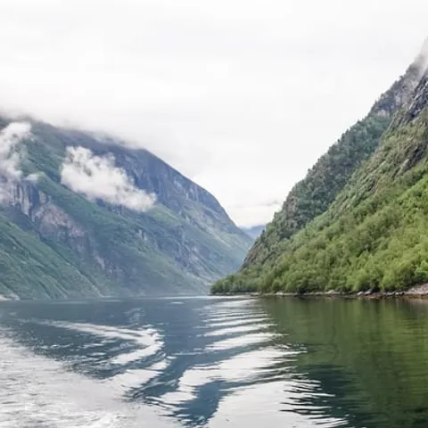 Steep fjord cliffs seen over a boat wake
