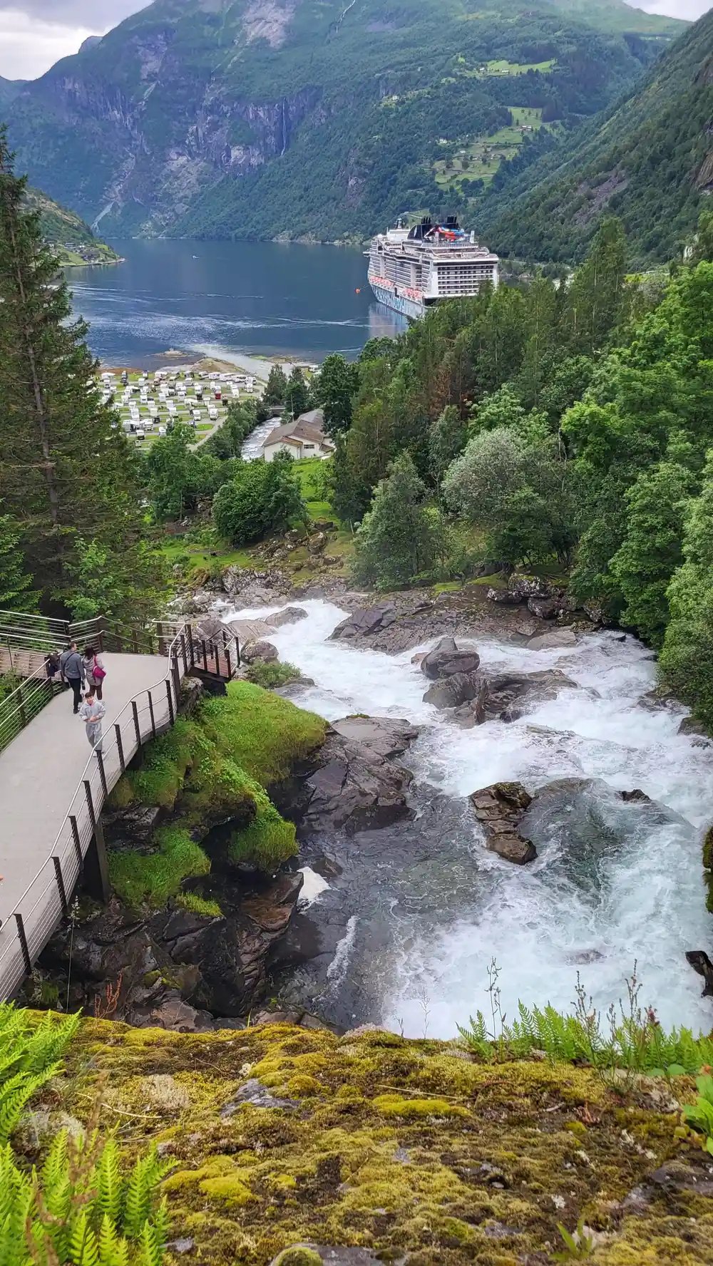 Large cruise ship docked at fjord with white water river