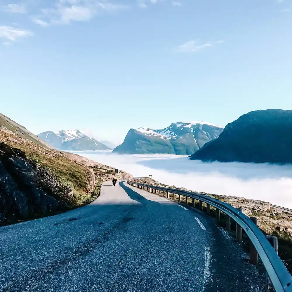 Mountain road curving above fog-filled valley with snow peaks
