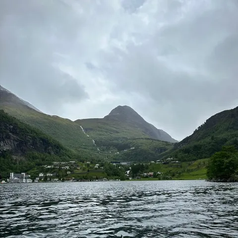Red kayak bow on calm fjord water below green mountains