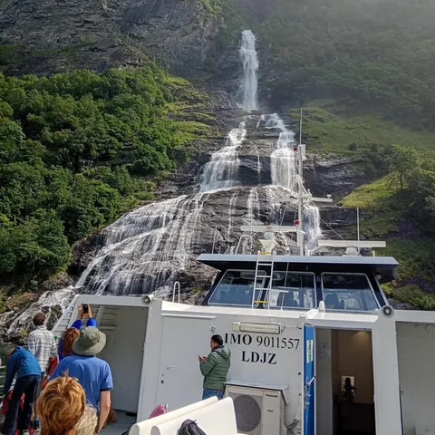 Sightseeing boat bow pointing at a waterfall in the fjord