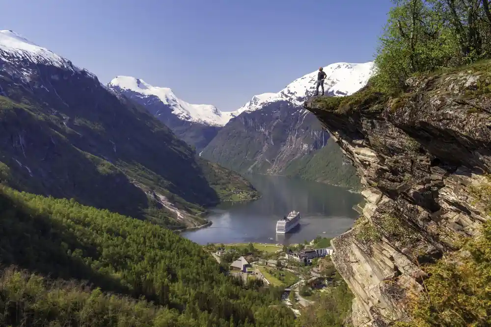 Steep green valley with cruise ship on narrow fjord below