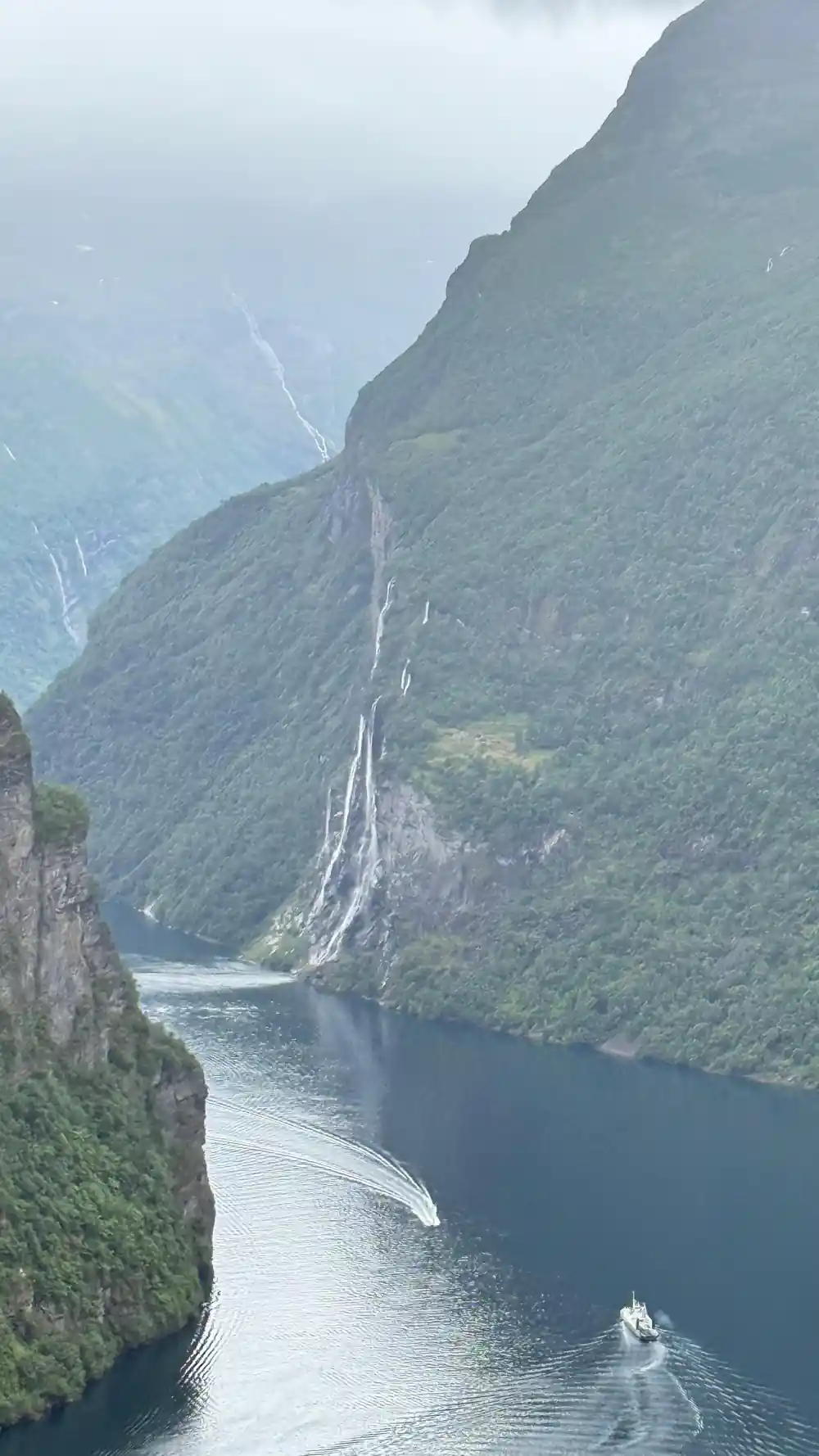 Steep mountain slope with distant waterfall and fjord water