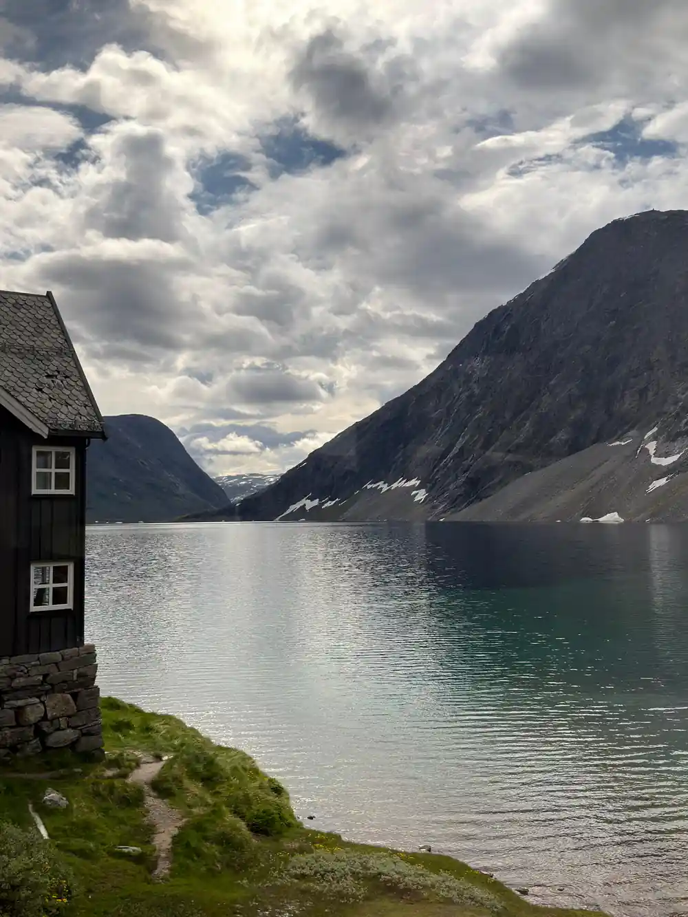 Stone cottage beside still alpine lake with mountain backdrop