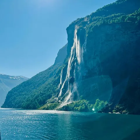 Sunlit cliff with a thin waterfall above deep blue water