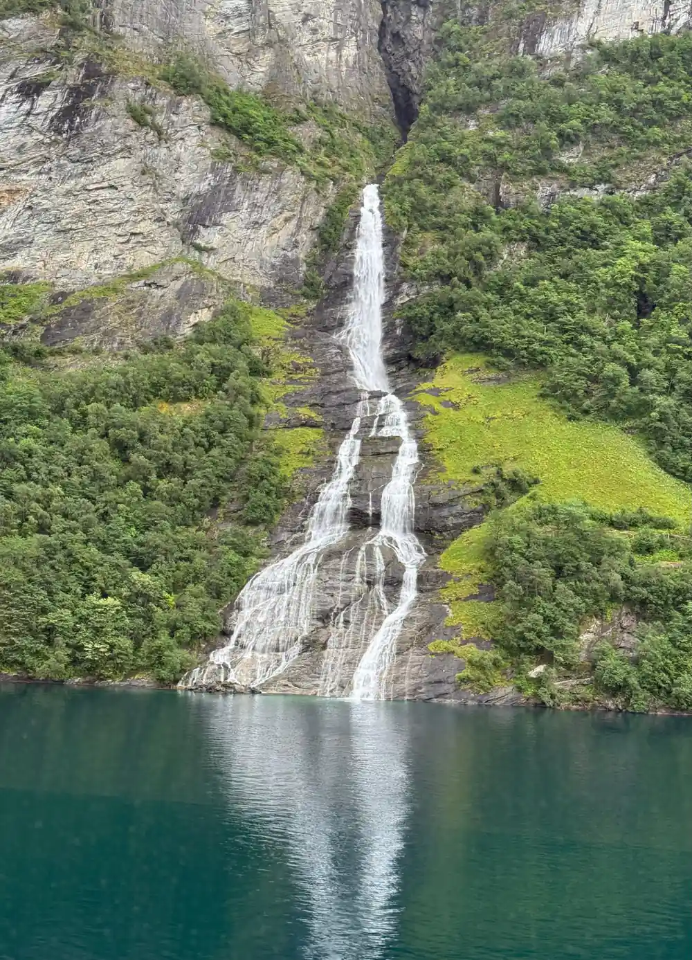 Tall waterfall cascading into turquoise fjord water