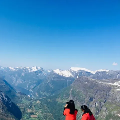 Two travellers at a viewpoint above snowy mountain peaks