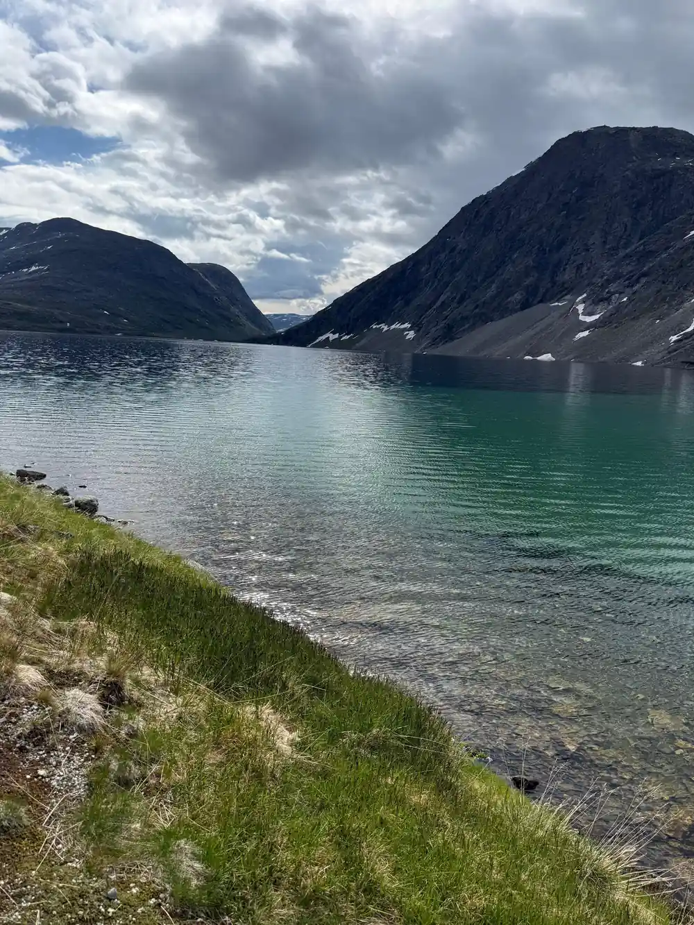 Turquoise fjord between steep mountain slopes with grass