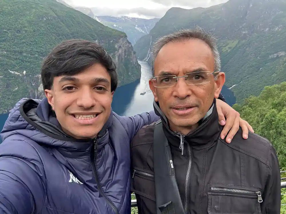 Two men smiling at viewpoint above cruise ship in fjord valley