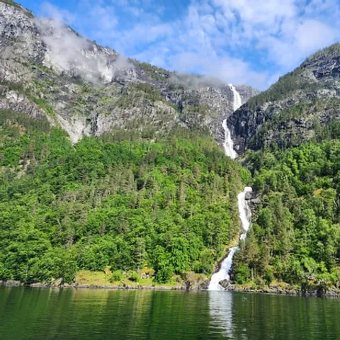 Waterfall dropping down a green slope into the Geirangerfjord