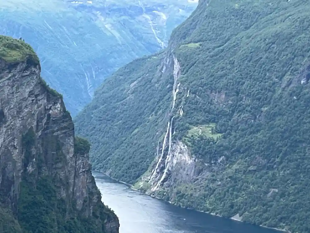 Waterfall cascading down forested cliff into blue fjord