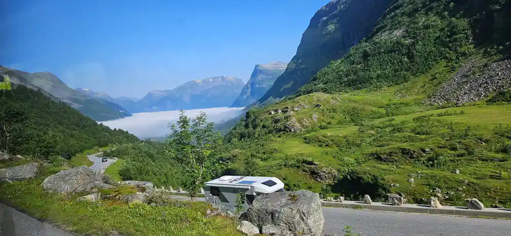 White van parked in green alpine meadow with lake and mountains